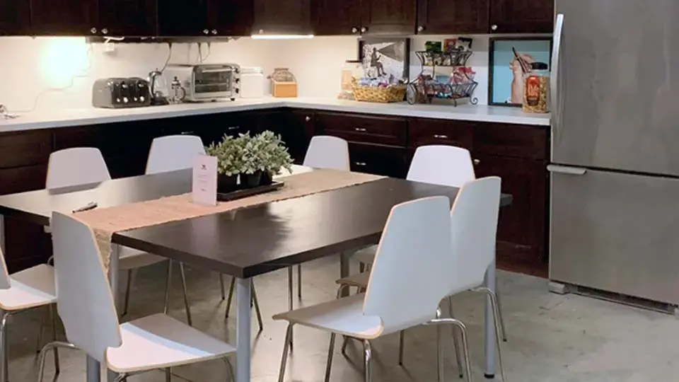 Client lounge with a dining table, white chairs, and a kitchenette beside the studio stage