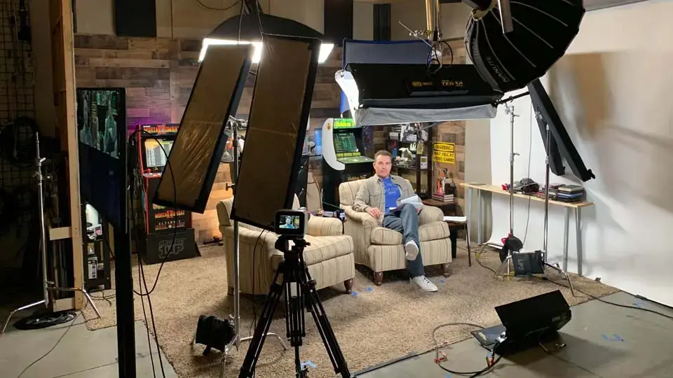 Two-person interview in a red-walled set with cameras and portable sound treatment