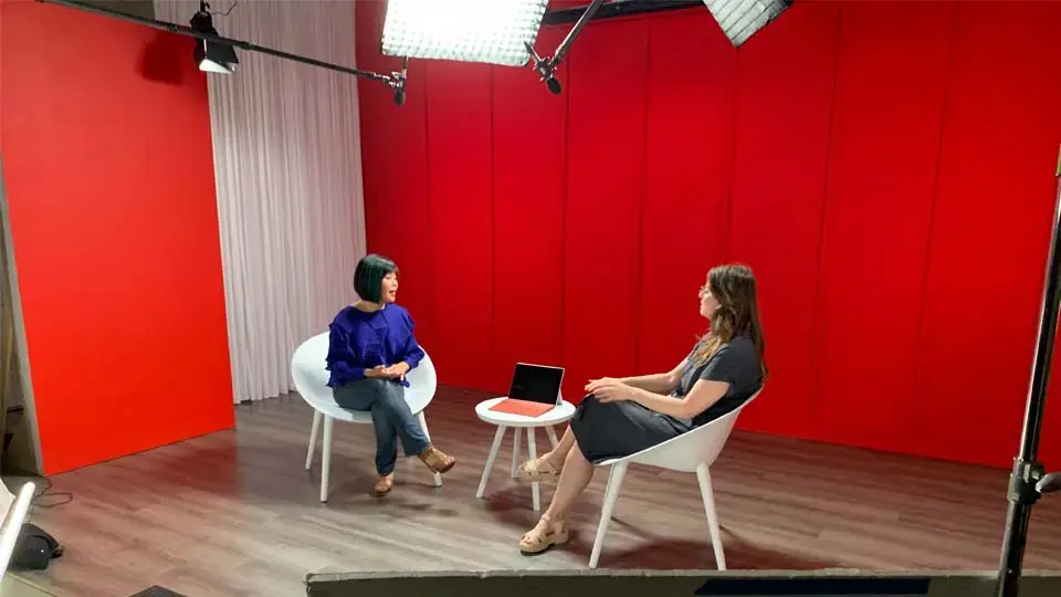 Two people seated on a green-screen stage in the studio’s large cyclorama space